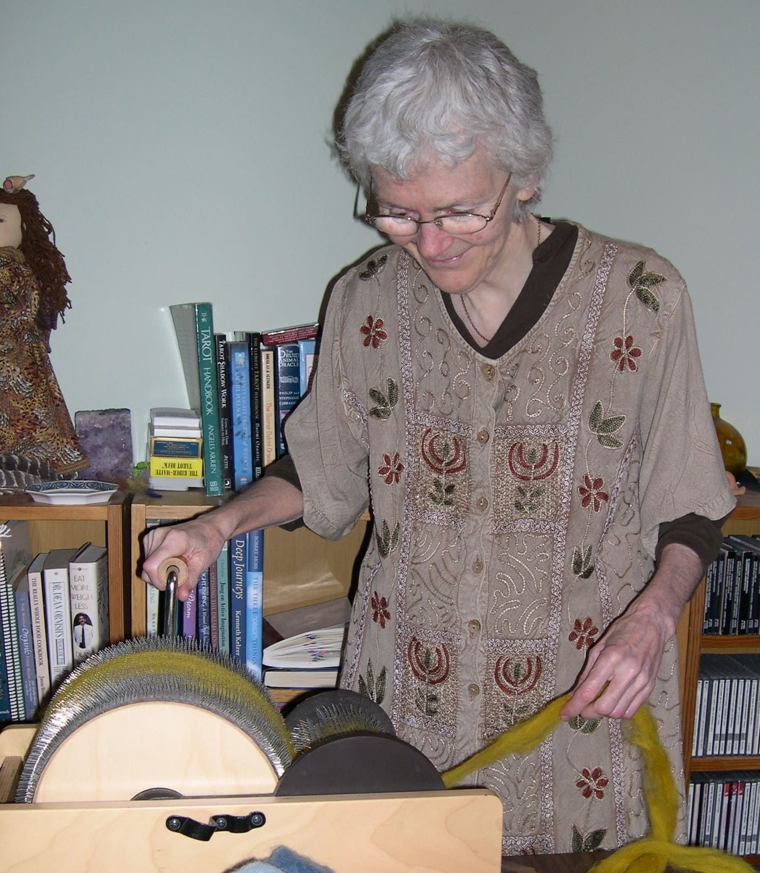 A person hand carding wool dyed with marigold flowers using two paddle-shaped hand cards, transferring fiber between the two tools to open and align it