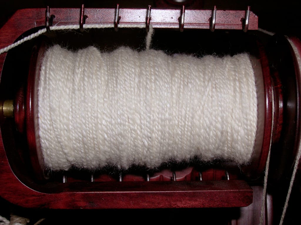 Hands spinning Pygora fiber on a drop spindle, twist running up the drafted fiber as the spindle hangs below