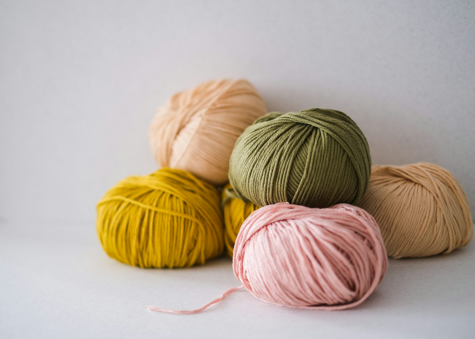 Five neatly wound center-pull yarn balls in peach, olive green, mustard, pink, and tan, stacked together on a plain white background