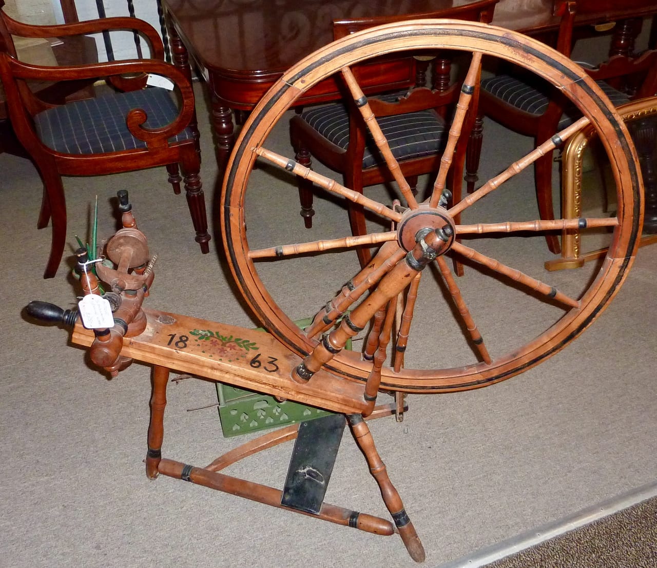An antique Scandinavian spinning wheel in an antique shop, showing the large drive wheel, flyer-bobbin assembly on an upright castle frame, and carved wooden details of the legs and uprights