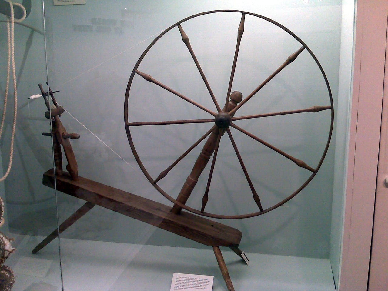 A spinning wheel showing the flyer-bobbin assembly mounted above the drive wheel, with the orifice visible at the front of the flyer housing