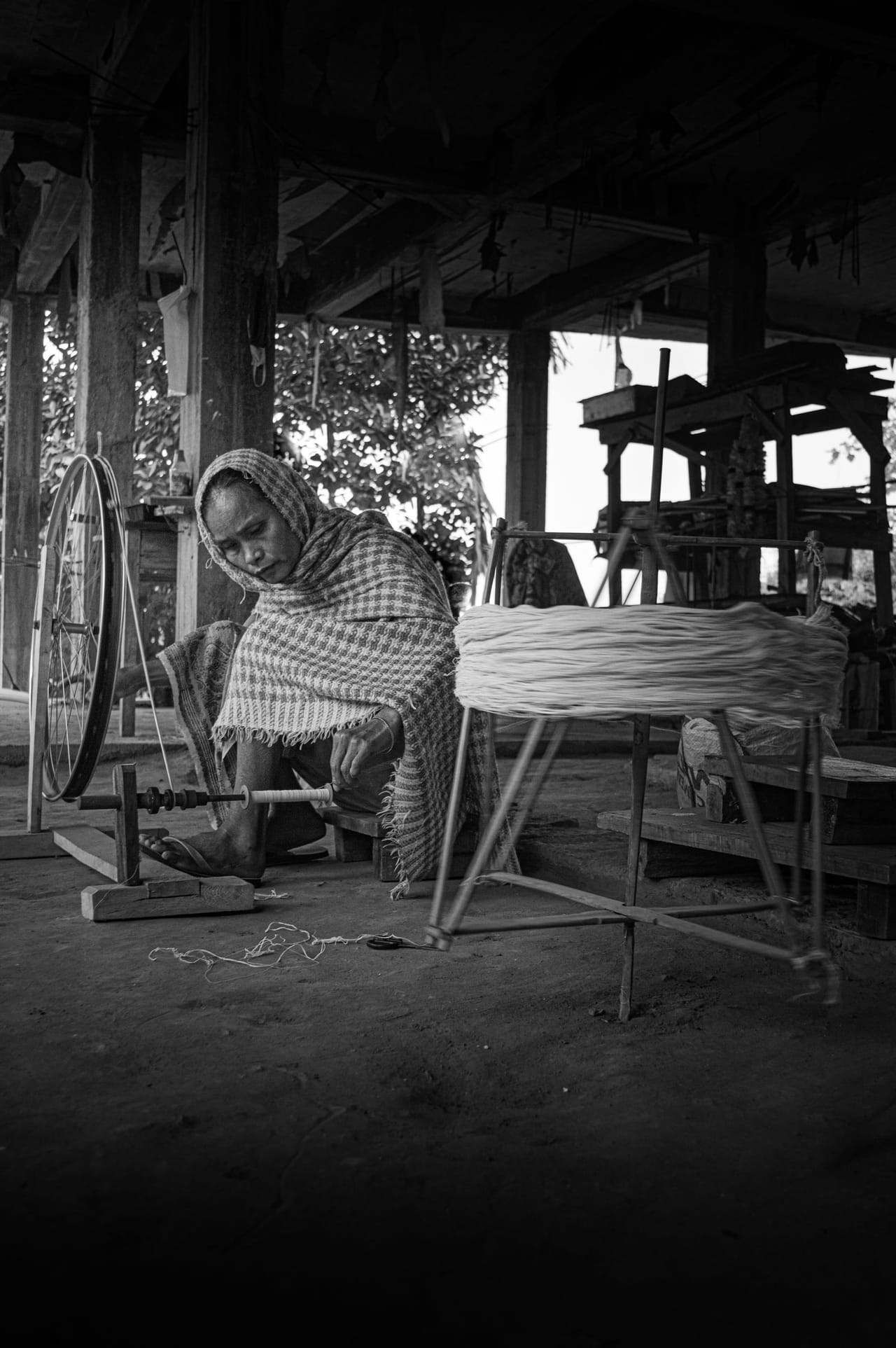 A woman spinning fiber on a spinning wheel in a workshop setting, her hands drafting the fiber as the wheel turns