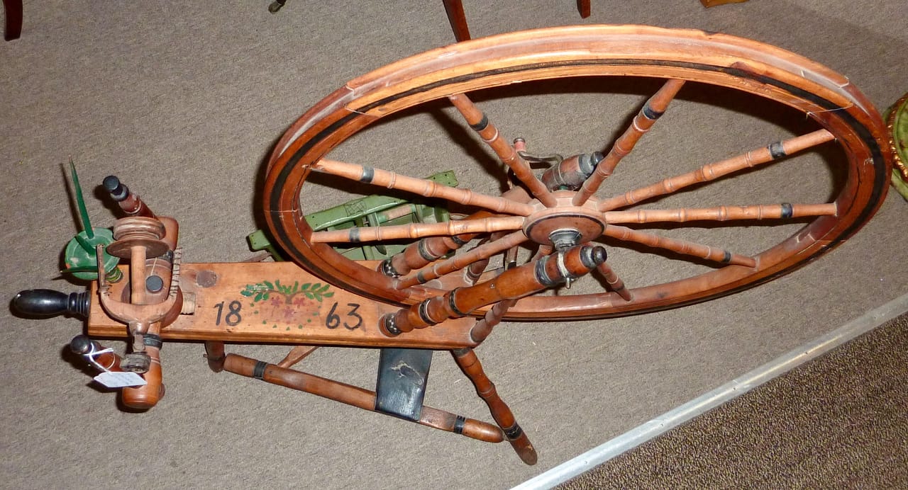 Top-down view of an antique Scandinavian Saxony spinning wheel showing the woodworking construction in detail, with the drive wheel at the top, the flyer-bobbin housing to the left, and the carved wooden uprights connecting them across the frame