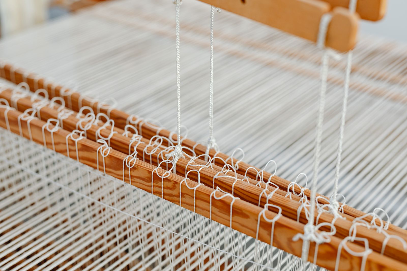Close-up of warp and weft threads interlacing on a floor loom, showing the weave structure forming as the shuttle passes through the shed between parallel warp ends