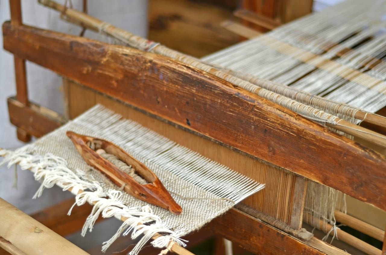Close-up of warp threads running through the heddles of a floor loom, showing the parallel warp ends under tension with the heddle frames visible above