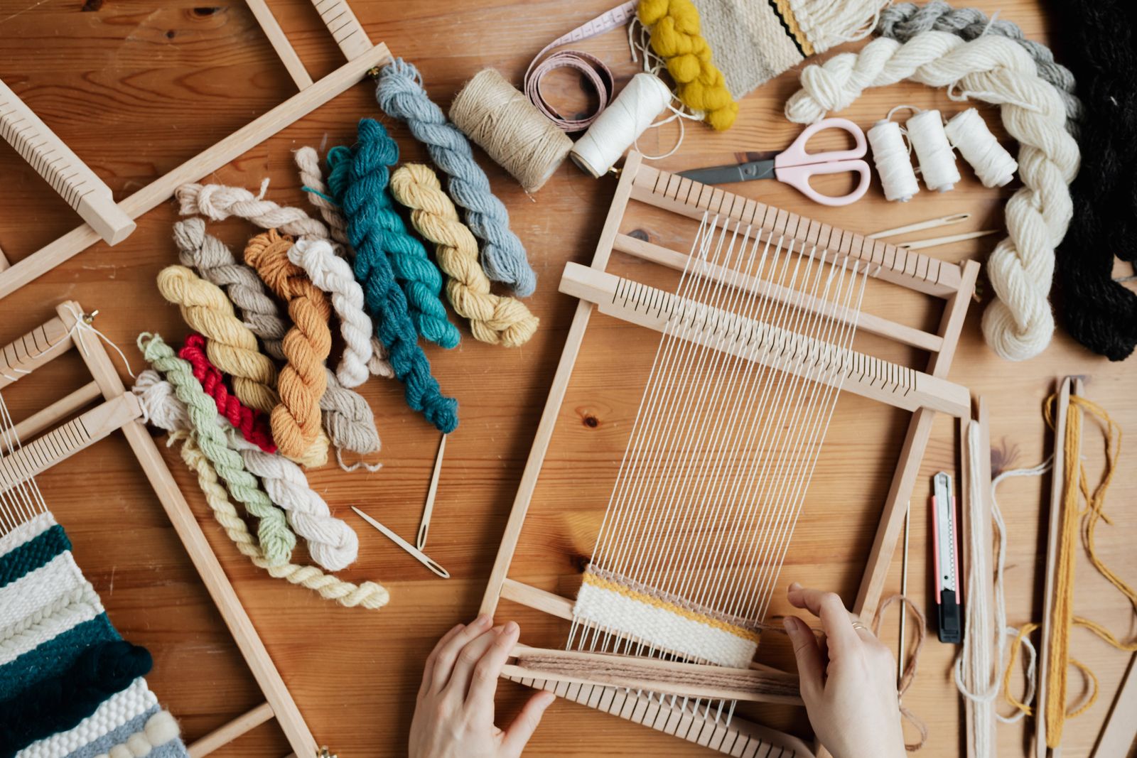 Close-up of hands weaving on a floor loom showing warp and weft threads interlacing on a working loom