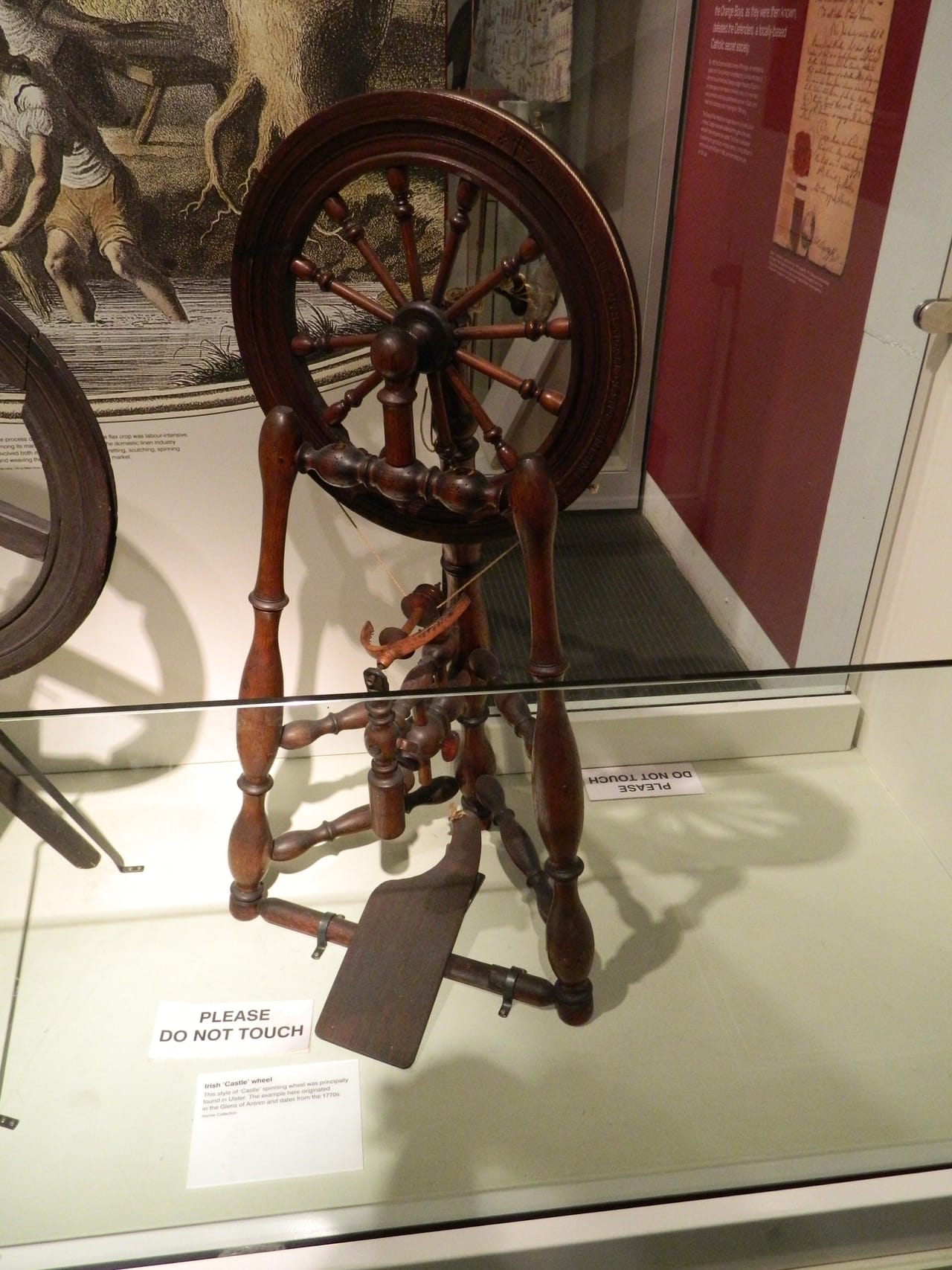 An Irish castle-style spinning wheel showing the vertical upright frame, double treadle, and flyer assembly typical of castle wheel design