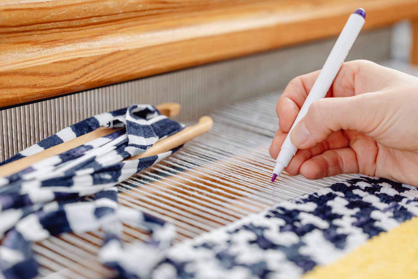 Hands threading yarn through the slot and hole pattern of a rigid heddle reed on a wooden loom