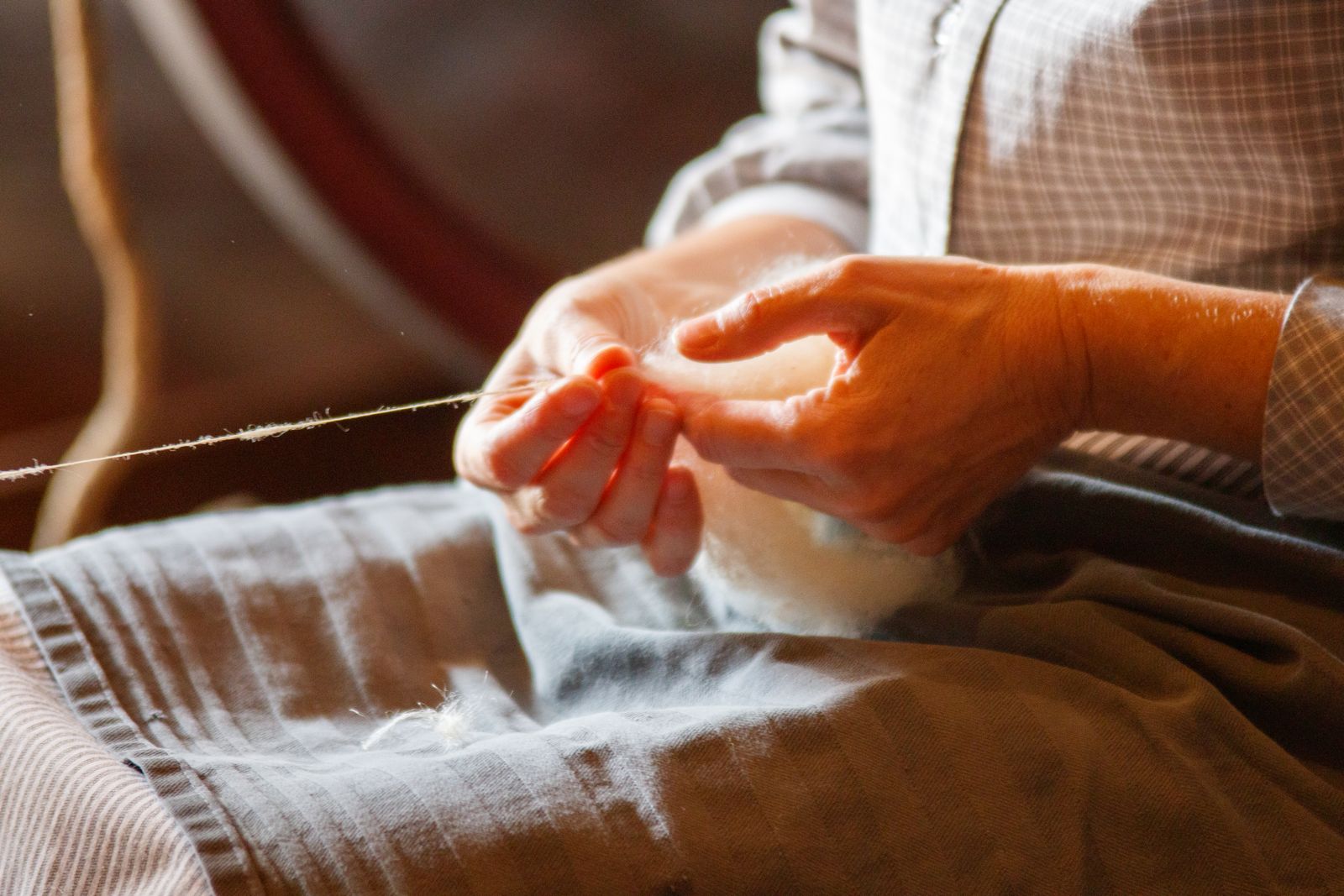 Close-up of hands drafting and spinning wool fiber into yarn, showing the fundamental drafting skill shared by both e-spinners and treadle spinning wheels