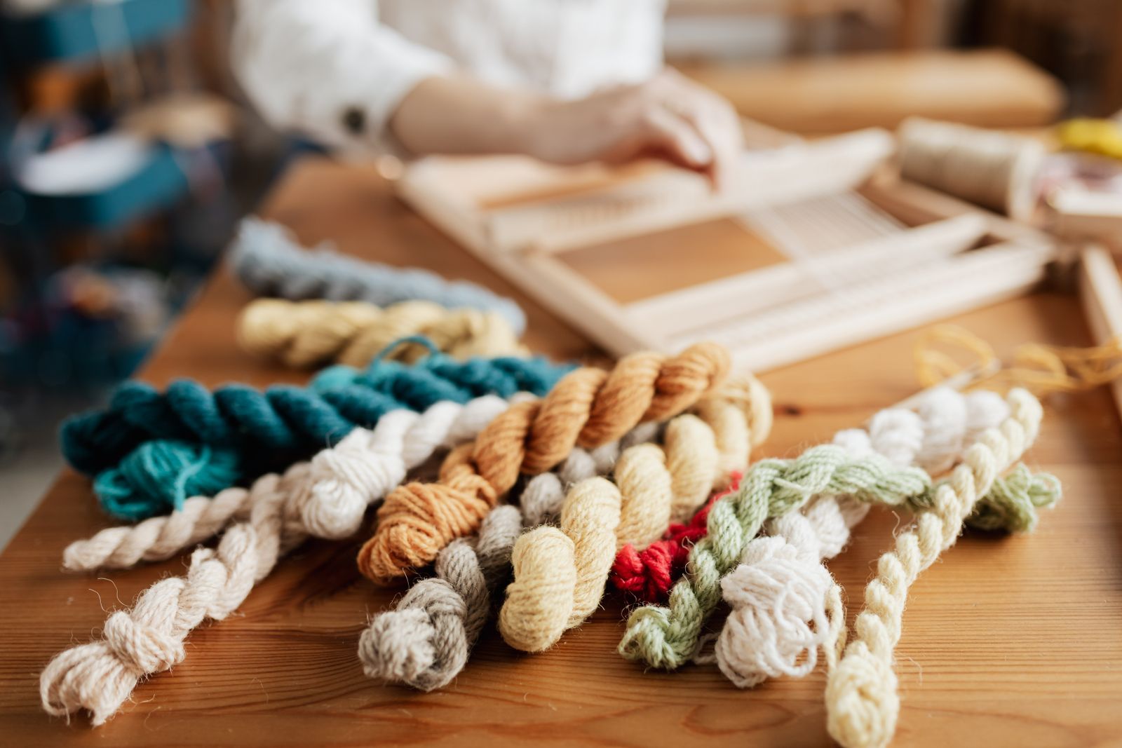 Colorful handspun yarn skeins in teal, amber, cream, sage and red arranged on a wooden studio table, showing the finished output of a spinning session