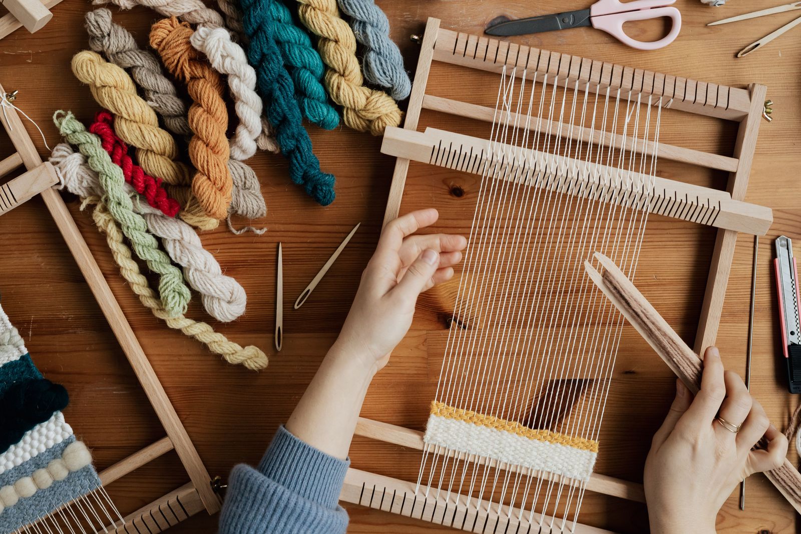 Overhead view of hands weaving colorful yarn on a small wooden hand loom