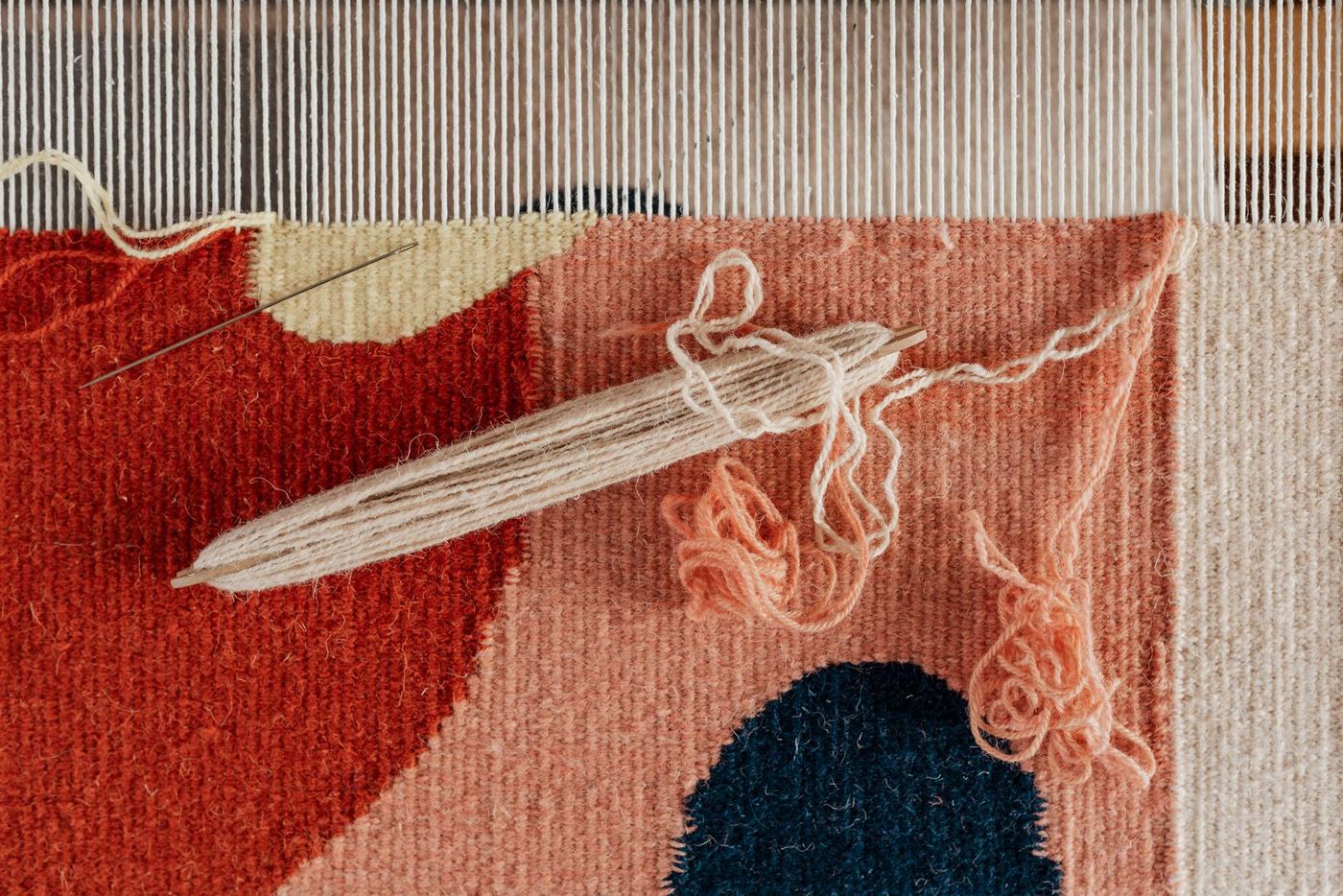 Close-up of an unfinished weft-faced tapestry on a small hand loom, a wooden shuttle resting across the warp