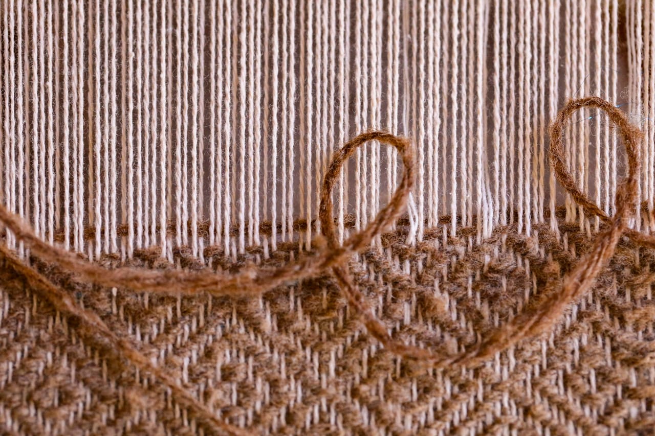 A wool string loom at a pioneer village settlement showing 19th-century weaving techniques with wooden frame, tensioned warp, and cloth in progress on the breast beam