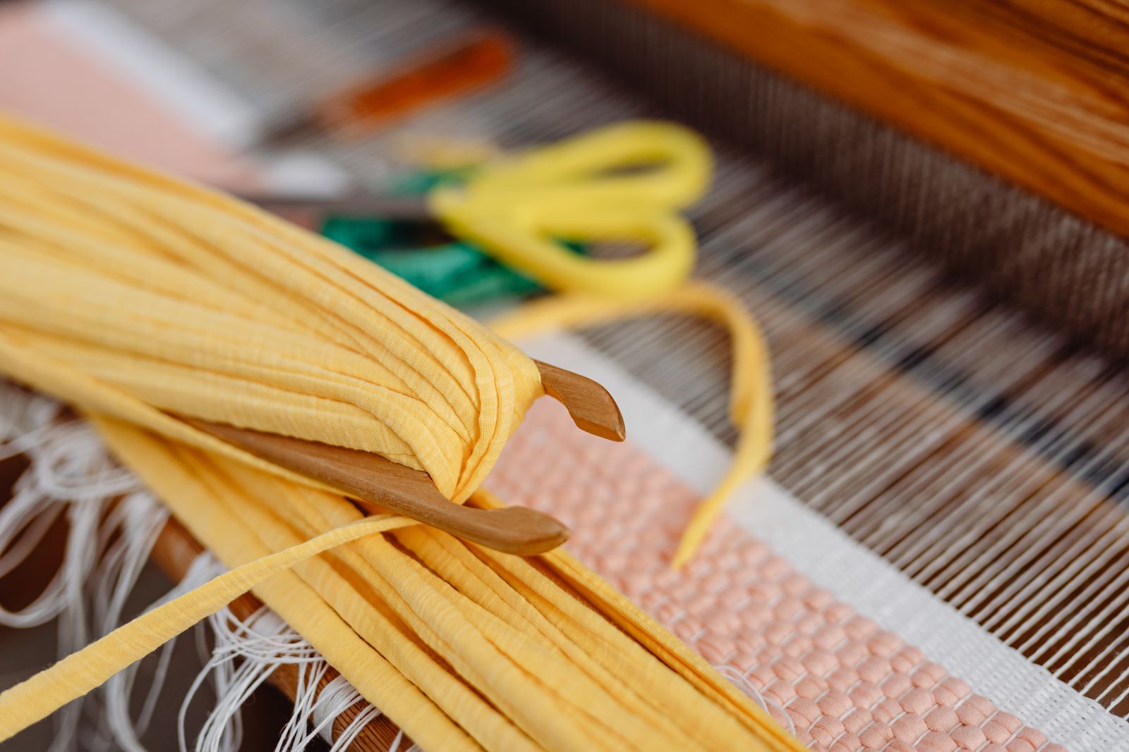 Hands threading warp yarn through a rigid heddle reed on a small table loom, with a ball of yarn sitting nearby