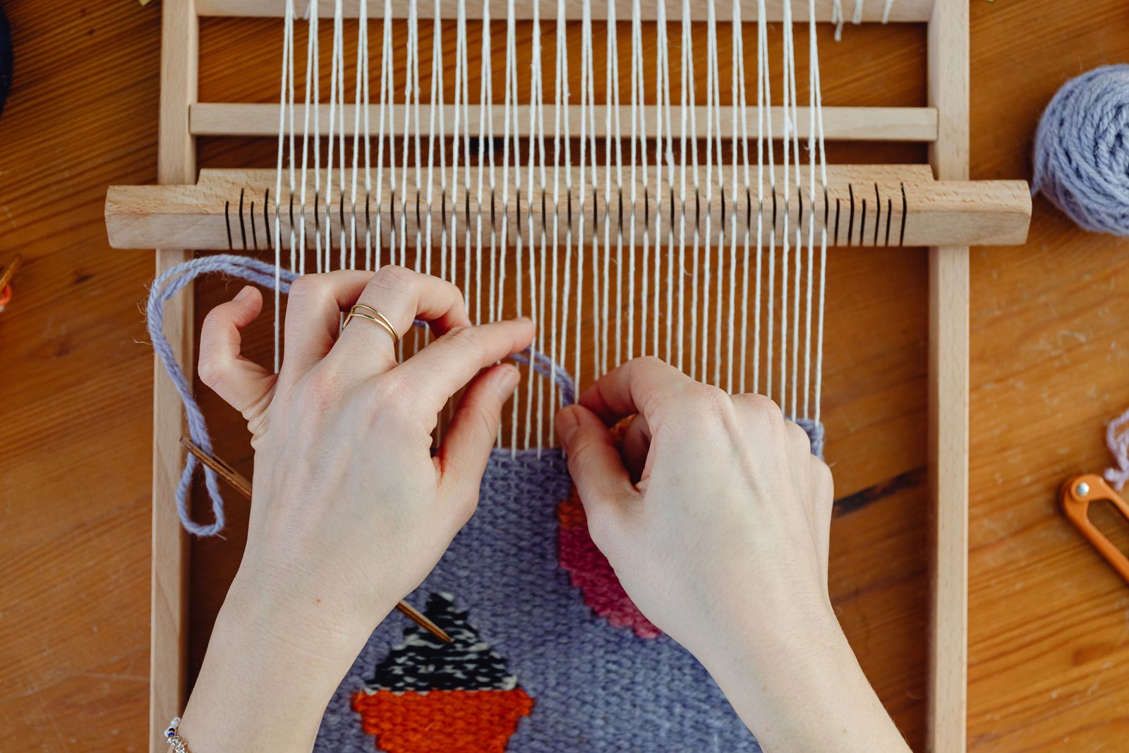 Close-up of hands beating weft on a small wooden loom with woven cloth building up below the reed