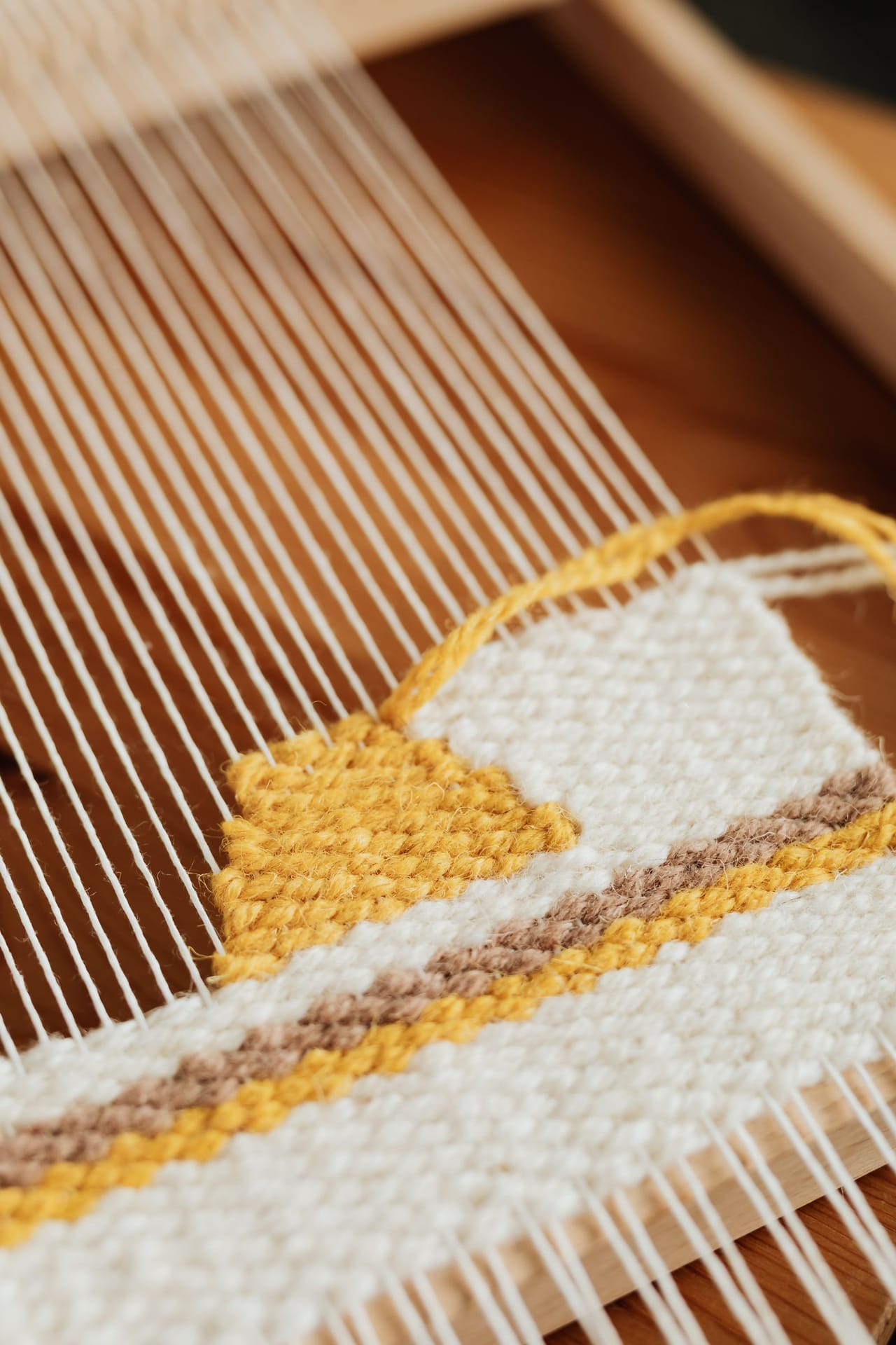 Close-up of colorful warp threads wound under tension on a wooden floor loom, showing the parallel arrangement of warp ends before threading through heddles and reed