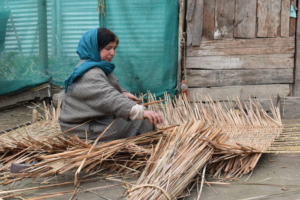 A woman weaving Wagoo traditional Sudanese cloth on a narrow traditional handloom, the finished cloth building in bands of color
